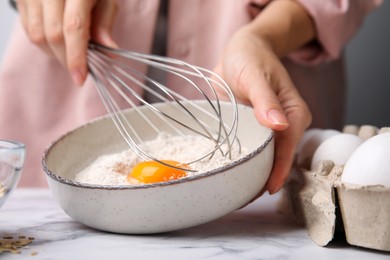 Woman mixing egg with flour at white marble table in kitchen, closeup. Cooking oatmeal dough
