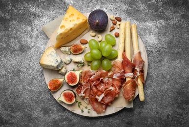 Photo of Board with delicious figs, cheese, grapes and bread with proscuitto on grey table, top view