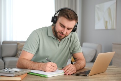 Young man taking notes during online webinar at table indoors