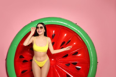 Young woman with stylish sunglasses near inflatable mattress against pink background