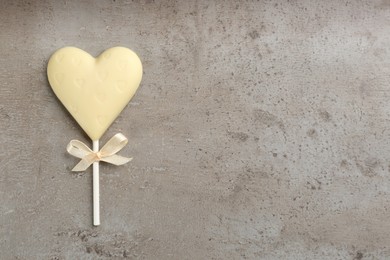 Chocolate heart shaped lollipop on grey table, top view. Space for text