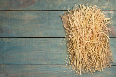 Heap of dried hay on light blue wooden background, flat lay. Space for text