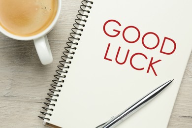 Notebook with phrase GOOD LUCK, pen and cup of coffee on white wooden table, flat lay