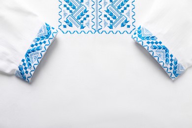 Beautiful white shirt with light blue Ukrainian national embroidery, top view. Space for text