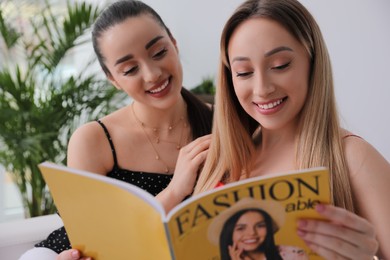 Happy women reading fashion magazine together indoors