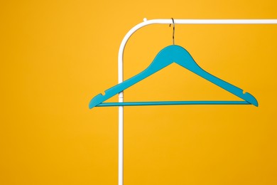 Blue clothes hanger on metal rack against yellow background