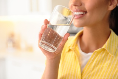 Young woman drinking pure water from glass in kitchen, closeup