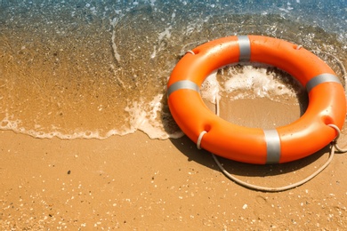 Orange life buoy on sand near sea. Emergency rescue equipment