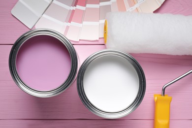 Photo of Cans of pink and white paints, roller with palette on color wooden table, flat lay