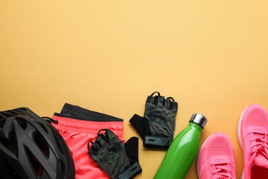 Photo of Flat lay composition with different cycling accessories and clothes on pale orange background, space for text