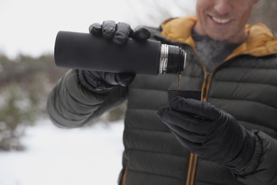 Man pouring hot drink from thermos into cap outdoors on snow day, closeup