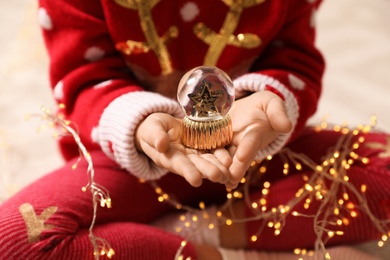 Little girl in red Christmas sweater holding snow globe, closeup