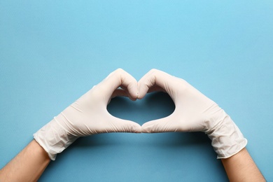 Person in medical gloves showing heart gesture against blue background, closeup of hands