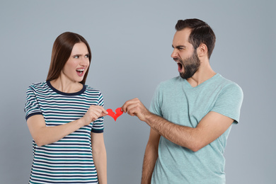 Couple tearing paper heart on light grey background. Relationship problems