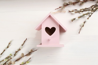 Beautiful bird house with heart shaped hole and willow branches on white wooden background. Spring flat lay composition