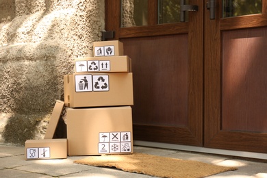 Cardboard boxes with different packaging symbols near entrance, space for text. Parcel delivery