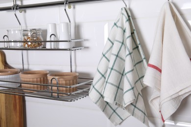 Photo of Different kitchen towels hanging on hook rod and shelves with bowls indoors
