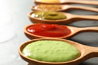 Set of wooden spoons with different delicious sauces on grey table, closeup
