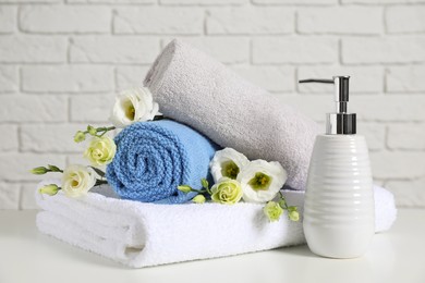 Clean soft towels with flowers and soap dispenser on table near white brick wall
