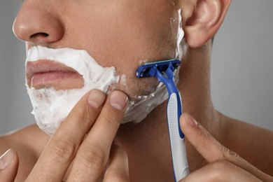 Man shaving with razor on grey background, closeup