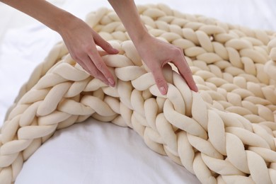 Woman folding chunky knit blanket on bed at home, closeup