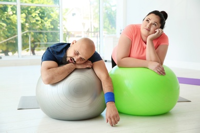 Tired overweight man and woman resting on fitness balls in gym