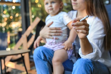 Photo of Mother with cigarette and child outdoors, focus on hand. Don't smoke near kids