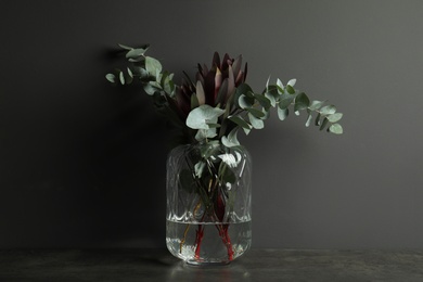 Photo of Bouquet of protea flowers and eucalyptus branches in glass vase on table against black background