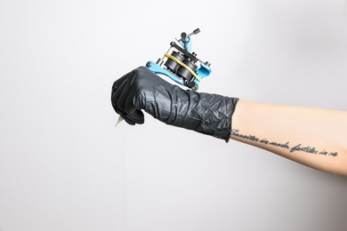 Professional tattoo artist with machine on white background, closeup