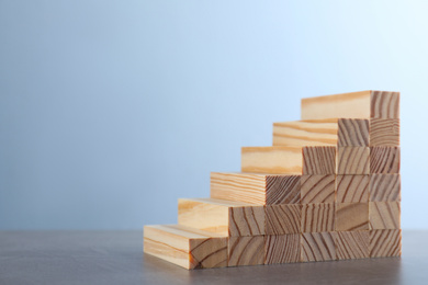 Photo of Steps made with wooden blocks on grey table, space for text. Career ladder