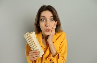 Photo of Emotional young woman with delicious shawarma on grey background