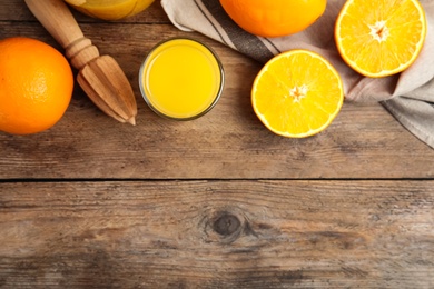 Fresh ripe oranges, reamer and juice on wooden table, flat lay. Space for text