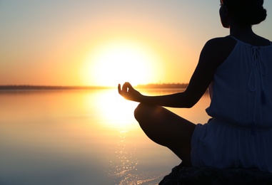 Woman practicing yoga near river on sunset, closeup. Healing concept
