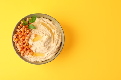 Photo of Bowl of tasty hummus with chickpeas and parsley on yellow background, top view. Space for text