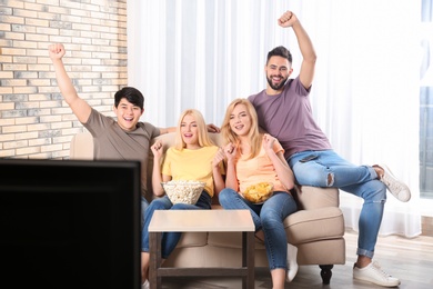 Photo of Young friends with snacks watching TV on sofa at home
