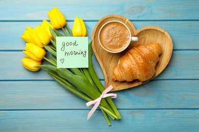 Cup of aromatic coffee with croissant, beautiful yellow tulips and Good Morning note on light blue wooden table, flat lay