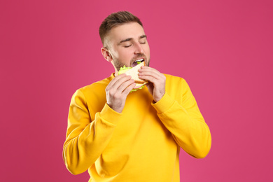 Photo of Young man eating tasty sandwich on pink background
