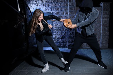 Woman fighting with thief while he trying to steal her bag near van at night. Self defense concept