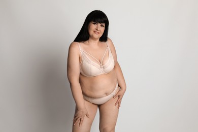 Beautiful overweight woman in beige underwear on light background. Plus-size model