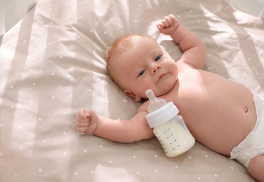 Cute healthy baby with bottle of milk lying in cot