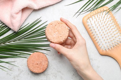 Woman holding solid shampoo bar at light grey table, top view. Hair care