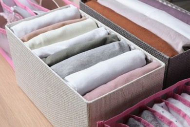 Textile cases with folded clothes on wooden background, closeup. Vertical storage
