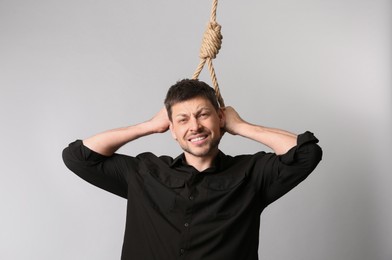 Depressed man with rope noose on neck against light background