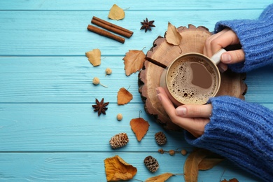 Photo of Woman with cup of hot drink at light blue wooden table, top view. Cozy autumn atmosphere