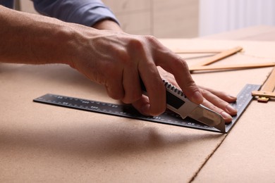 Man cutting chip board with utility knife and ruler indoors, closeup