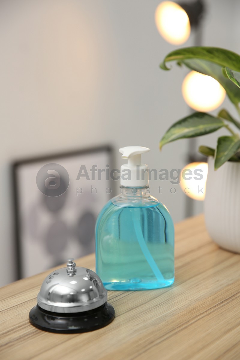 Photo of Dispenser bottle of antiseptic gel and service bell on reception desk in hotel