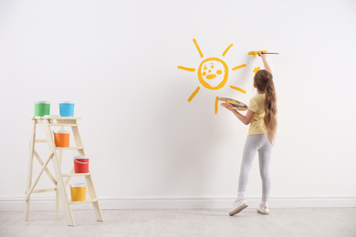 Little child painting sun on white wall indoors