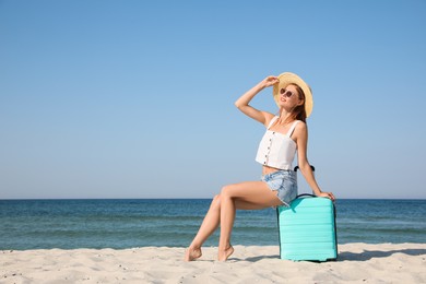 Beautiful woman with suitcase on sandy beach near sea