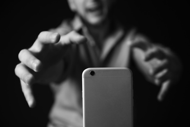 Emotional man reaching for smartphone on dark background, black and white effect. Addiction concept