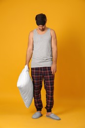 Man with pillow and eye mask in sleepwalking state on yellow background